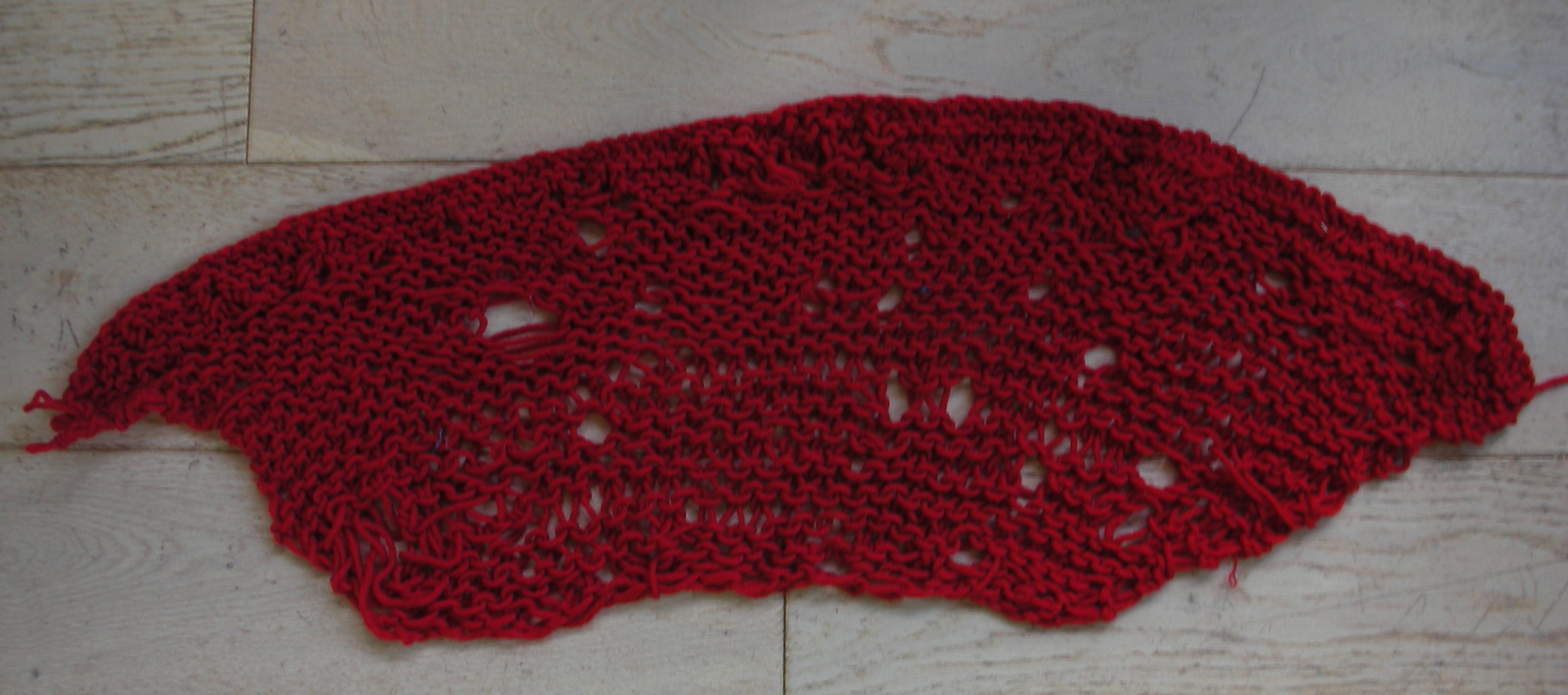 A knit trapezoid shaped scarf with lots of holes and a significantly looser tension at the bottom tham at the top, which is wider.